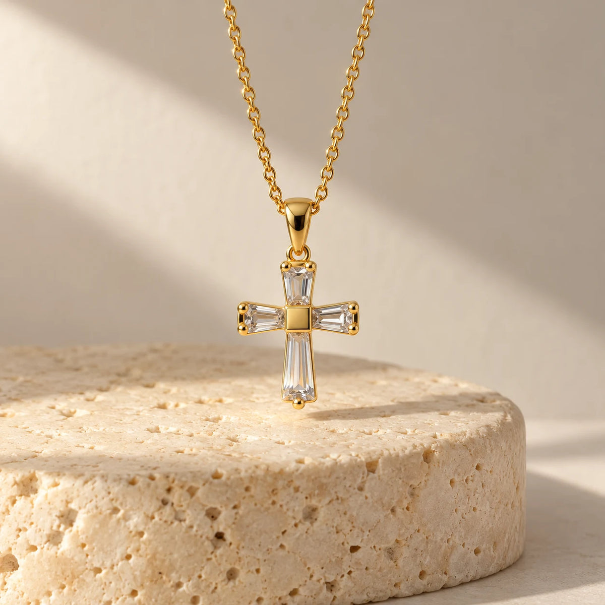 18K gold plated Haven Cross Necklace suspended over travertine