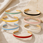 Seven color enamel cuff bracelets arranged on ivory linen and stone