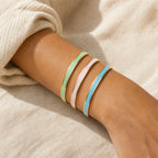Three continuous gold enamel cuff bracelets in green pink and blue worn together