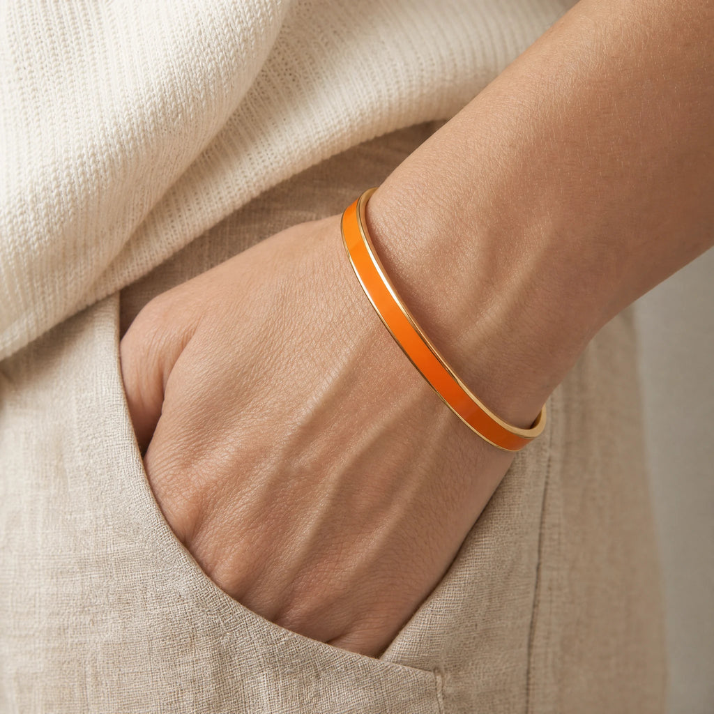 Orange enamel reminder cuff worn as one continuous band with a hand resting in a linen pocket