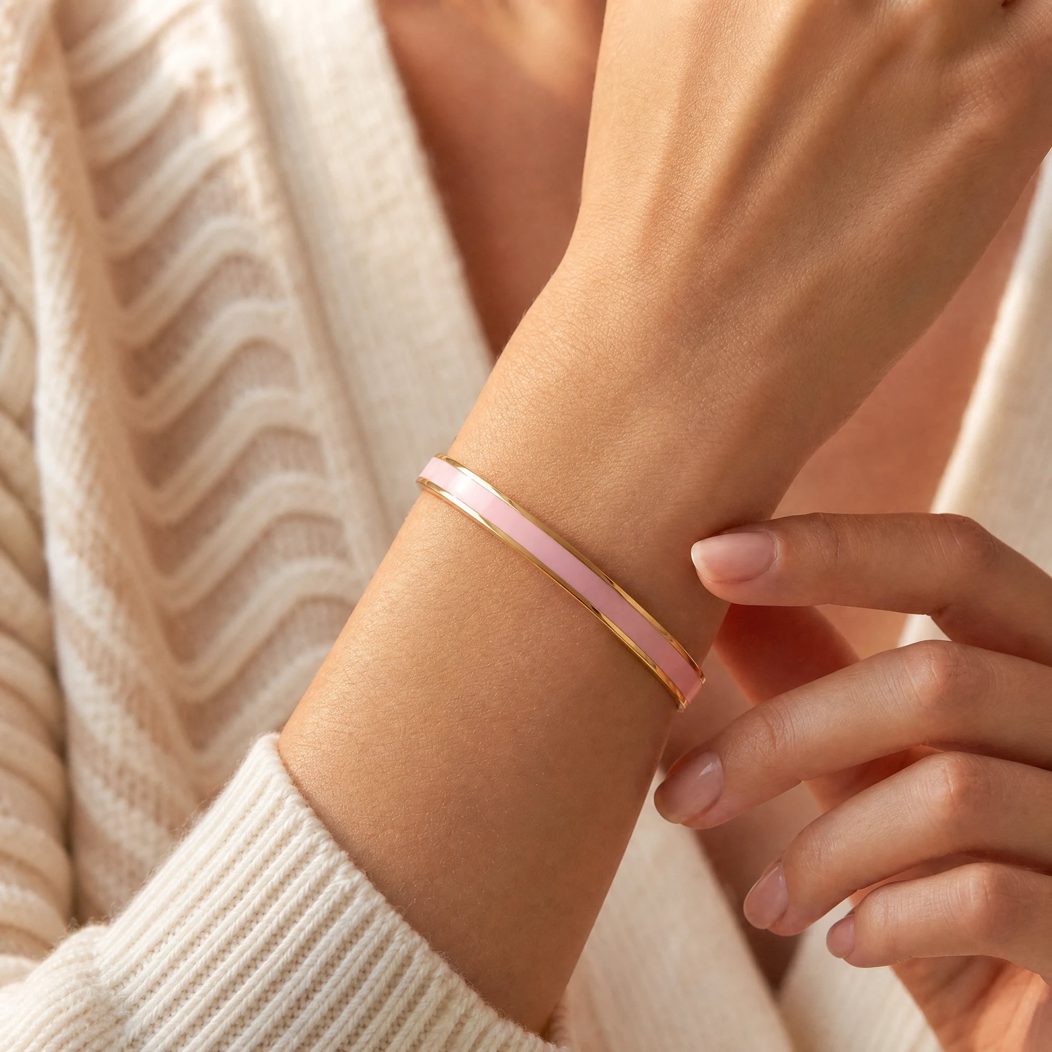 Woman gently adjusting a continuous pink enamel reminder cuff with soft ivory knitwear