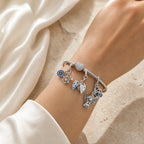 CALEO Heart & Geometric Clasp Snake Chain Bracelet lifestyle on ivory silk with Compass, Moon, Angel, and Celtic charms