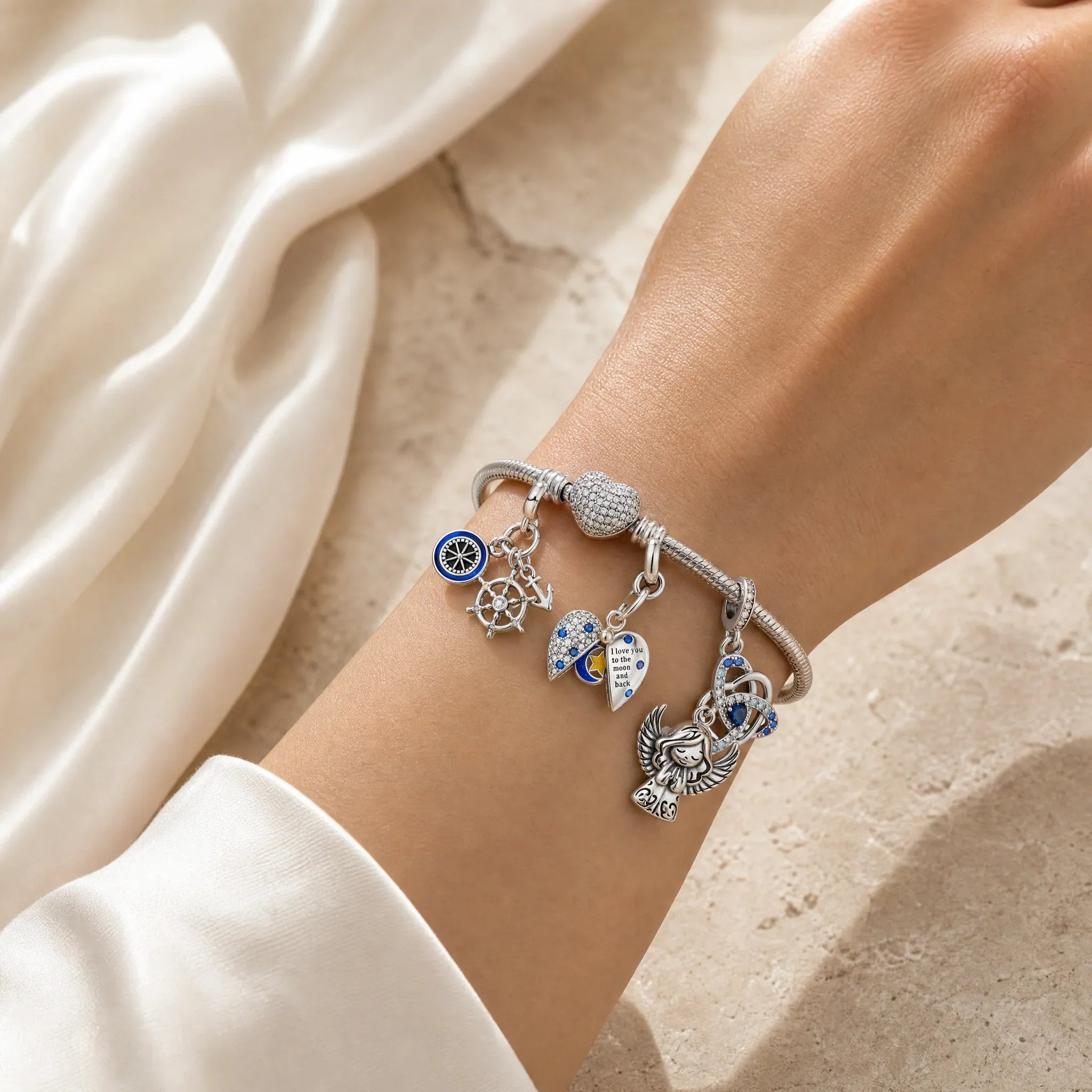 CALEO Heart & Geometric Clasp Snake Chain Bracelet lifestyle on ivory silk with Compass, Moon, Angel, and Celtic charms