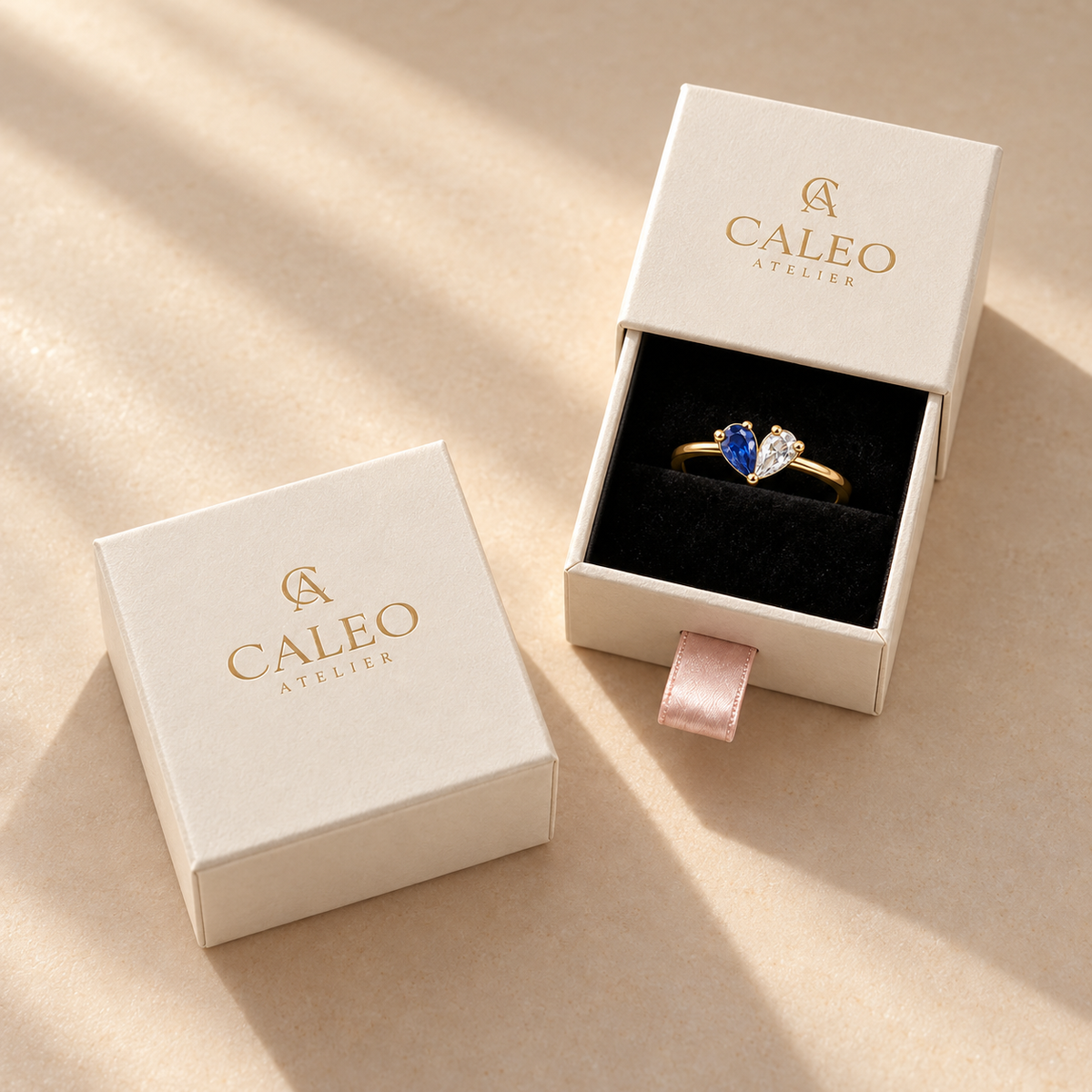 Gold-finish two-birthstone heart ring with blue and clear stones in a cream CALEO ATELIER gift box