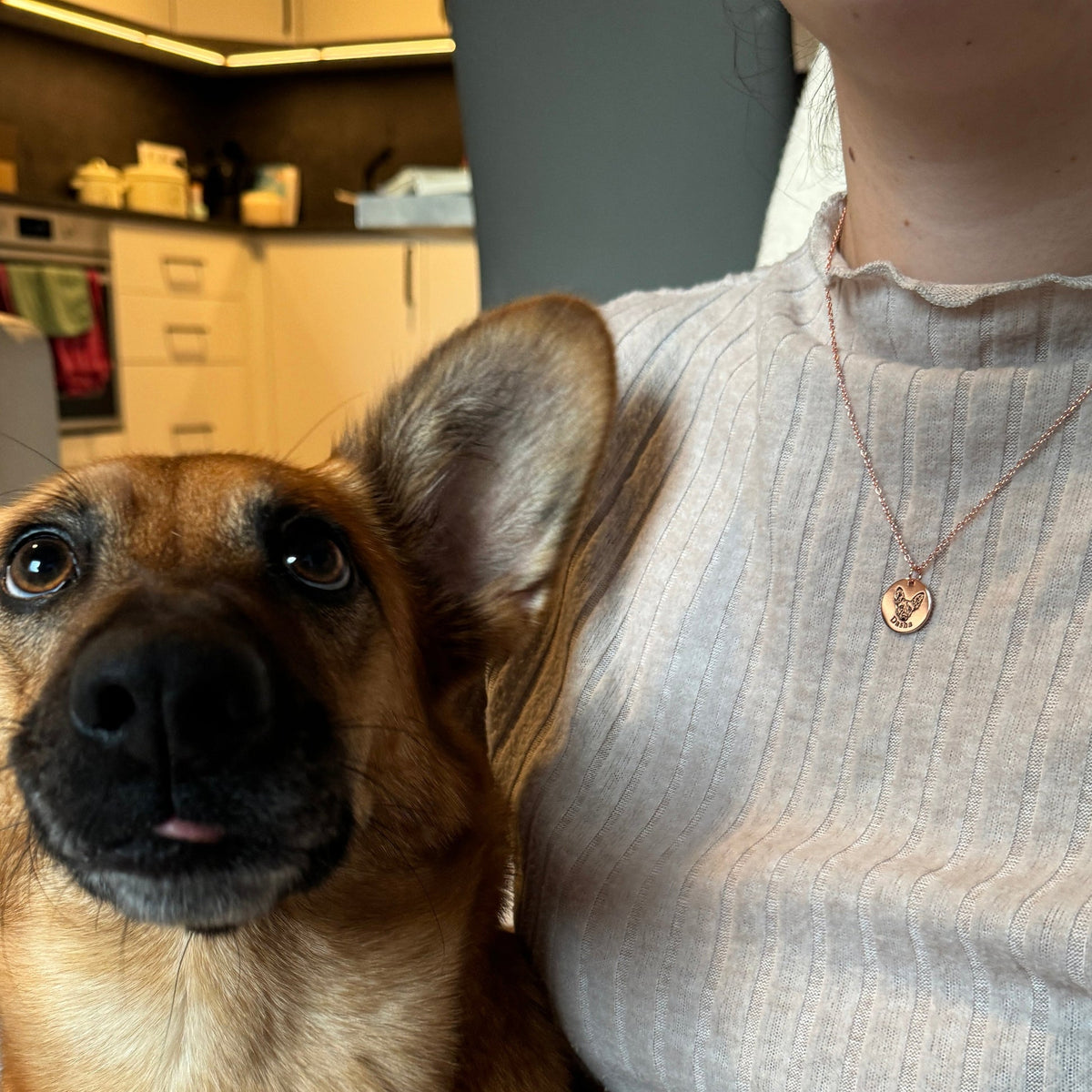 A pet parent wearing a rose gold custom pet face necklace beside their dog