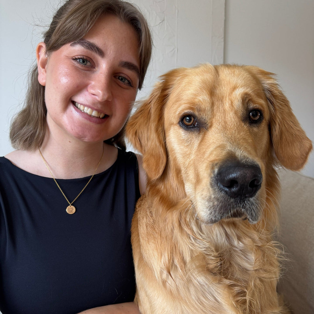 A smiling pet parent wearing a gold custom pet face necklace with their dog