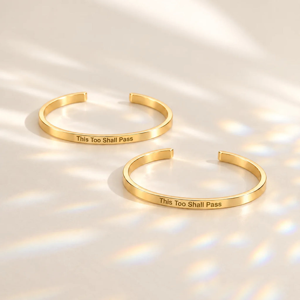 Two gold This Too Shall Pass Slim Cuffs with outside engraving in sunlight