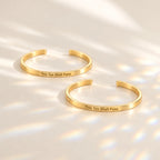Two gold This Too Shall Pass Slim Cuffs with outside engraving in sunlight